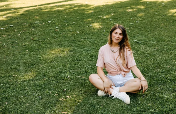 Young Woman Sitting Green Grass Park Looking Camera — Stock fotografie