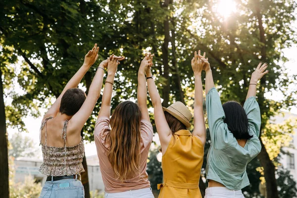 Four young anonymous women friends, in a park, holding hands up in the air.