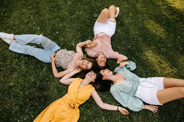 四个年轻女子坐在绿草上 在户外的一个公园里 微笑着 — 图库照片