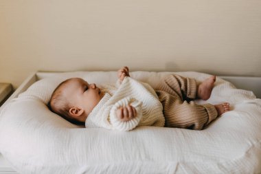 Kışlık giysiler giyen, kalın örülü bir süveter ve pantolon giyen bebek yuvasında yatıyor..