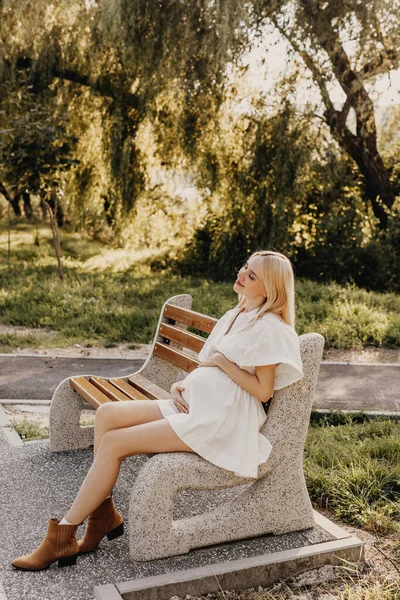 Těhotná Žena Bílých Šatech Sedí Lavičce Parku Slunečného Dne Drží — Stock fotografie
