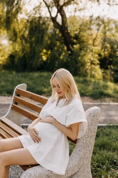 Беременная Женщина Белом Платье Смотрит Живот Сидит Скамейке Парке — стоковое фото