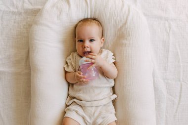 Bebek yuvasında yatıyor, süt şişesinden yiyor, gülümsüyor..