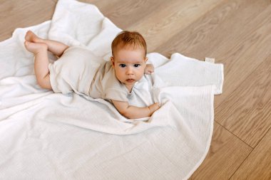 Bebek yerde beyaz bir muslin battaniyenin üzerinde uzanmış kameraya bakıyor..