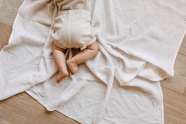 Closeup of barefoot baby lying on tummy on a white muslin blanket on the floor.