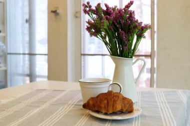 Pencere kenarında kahvaltı, kruvasan ve bir fincan sıcak kahve.