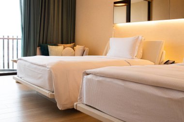 Modern ve iyi aydınlatılmış bir otel odası, beyaz çarşaflı iki rahat görünümlü yatak.