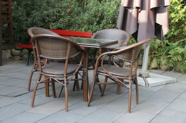 Açık hava hasır mobilya seti, içinde cam kapaklı bir piknik masası ve birkaç sandalye de var.. 