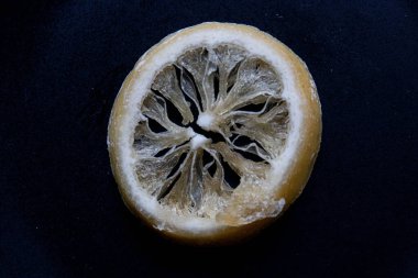 Koyu bir zemin üzerine katmanlanmış şeffaf kurutulmuş limon dilimlerinin yakın plan görüntüsü. Dilimlerin dokusu ve kırılganlığı korunmuş turunçgillerin doğal güzelliğini vurgular..