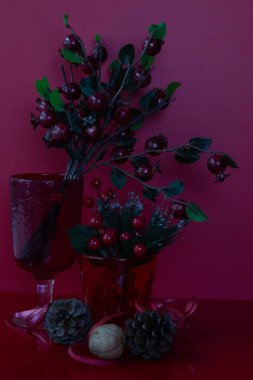 Kırmızı böğürtlen, yeşil yapraklar ve kırmızı ve pembe kurdelelerle birbirine bağlanmış çam kozalakları içeren dekoratif bir demet..