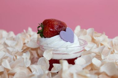 Taze, parlak bir çilek taçlandırır pürüzsüz bir tatlı bardağındaki krema girdabı, küçük mor bir kalp süslemesiyle vurgulanır..