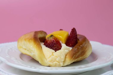 Altın renkli, parlak Danimarka pastası yumuşak kremayla doludur ve üzerinde çilek, üzüm ve parlak bir dilim şeftali gibi taze meyveler vardır..