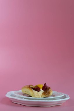 Altın renkli, parlak Danimarka pastası yumuşak kremayla doludur ve üzerinde çilek, üzüm ve parlak bir dilim şeftali gibi taze meyveler vardır..