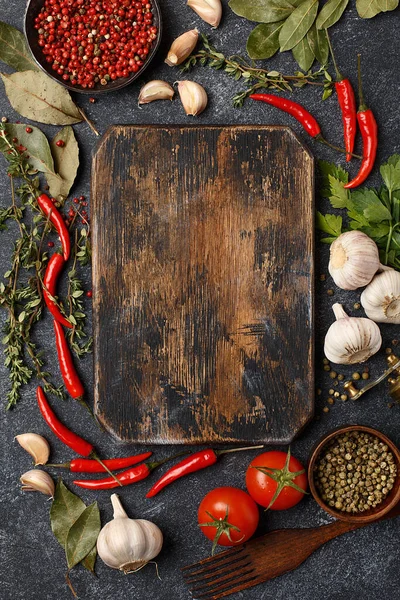 Various vegetables, herbs and spices with vintage wooden cutting board on dark concrete background. Top view with copy space. Frame composition, ingredients for cooking