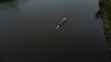 Aralarında dümencinin de bulunduğu sekiz kürek mürettebatı sakin bir nehirde antrenman yapıyor. Mürettebat dümenci ile birlikte teknenin arkasında düz bir çizgide..