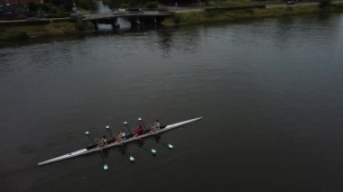 Bir grup kürekçi, Gent 'in sakin sularında zarif bir şekilde manevra yapıyor. Güneş ufkun altına batarken, sakin manzaranın üzerine resim gibi bir parıltı saçıyor..