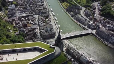 Dinant, Belçika 'nın dolambaçlı bir nehir boyunca uzanan pitoresk kasabasını gösteren hava manzarası. Çekim, şehrin eşsiz mimarisini yansıtıyor. Aralarında önemli bir kilise kulesi ve çevreleyen yeşil tepeler de var..