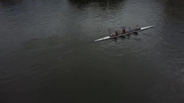 Altı kişilik bir kürek ekibi nehirde kürek çekerken görüldü. Mürettebat birlikte çalışıyor, kararlılıkla ilerliyorlar. Su sakin ve gökyüzü bulutlu. Huzurlu ve sakin bir atmosfer yaratıyor..