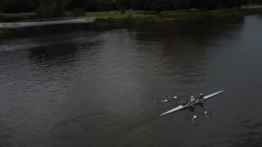 Bir kürek takımı bulutlu bir günde sakin bir nehirde pratik yapar. Kürekçiler yukarıdan görülür, tekneleri suda süzülür. Kürekler ritmik hareket ederken ekip çok çalışıyor. Huzurlu ve huzurlu bir sahne..
