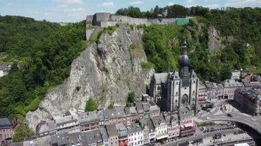 Belçika 'nın Dinant kentinin ikonik Kalesi ve Collegiate Kilisesi' nin şehir manzarası üzerinde yükselişe geçtiği hava manzarası. Meuse nehri vadide esiyor ve etrafındaki tepeler yemyeşil..