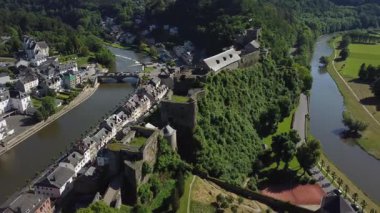 Bu video, Chateau Fort de Bouillon ve Belçika 'nın Bouillon kasabasının çarpıcı hava manzarasını sergiliyor. Yuvarlanan tepelerin, yemyeşil yeşilliklerin ve olay yerinde dolaşan dolambaçlı bir nehrin manzarasına tanık olun.