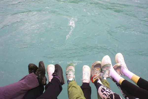 Young people hold legs over the water — Stock Photo, Image