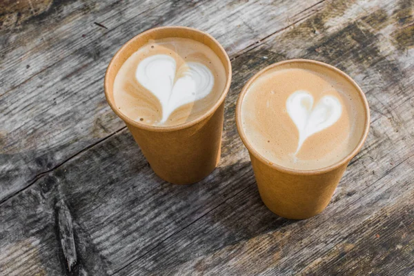 Dua cangkir kopi kertas dengan bentuk hati seni latte di latar belakang kuning — Stok Foto