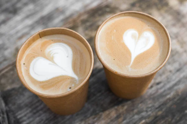 Dua cangkir kopi kertas dengan bentuk hati seni latte di latar belakang kuning — Stok Foto