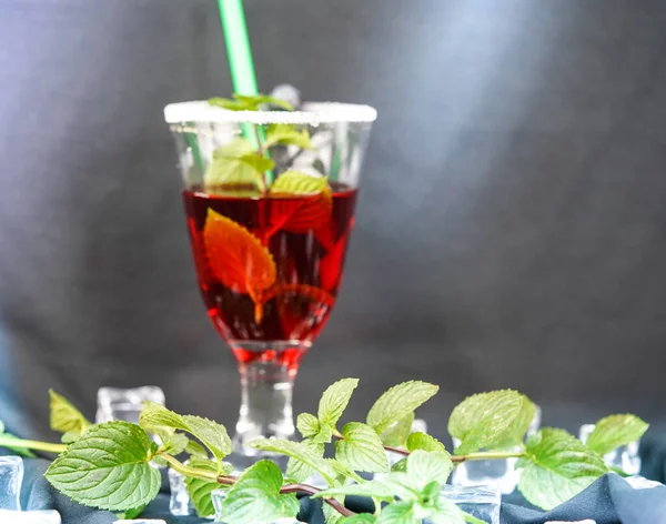 red cocktail with green mint leaves and ice rocks