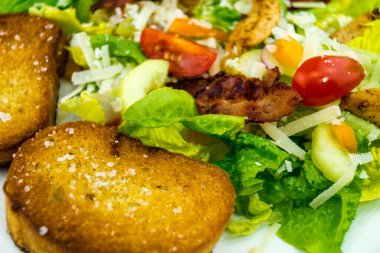 Izgara tavuk pastırmalı geleneksel sezar salatası ve tuzlu sarımsaklı ekmek.