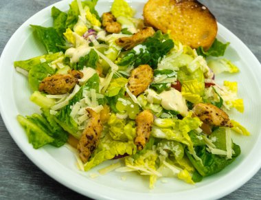 Izgara tavuk pastırmalı geleneksel sezar salatası ve tuzlu sarımsaklı ekmek.