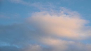 Beyaz ve pembe bulutlar açık mavi bir gökyüzünde hareket eder. Görüntü daha büyük bir bulutu görüntülemek için yakınlaştırılır.