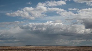 Beyaz ve gri bulutlar, hasat edilmiş bir çiftlik arazisinin üstündeki sonbahar gökyüzünde çalkalanıyor. Gölgeler tarlada hareket eder.