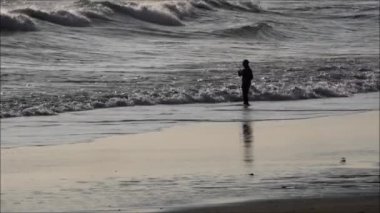 Silhouette Fisherman fishing on the beach in the front of big wave