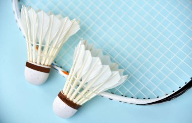 Badminton Shuttelcock ve raketi arka plan olarak açık mavi renkte izole edilmiş.