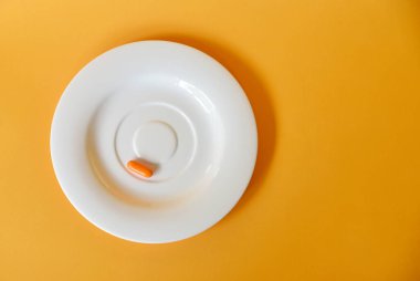 Sarı zemin üzerinde bir tablet C vitamini izole edilmiş küçük beyaz tabak.