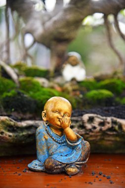 Bulanık bonsai ağacı arkaplanlı küçük ve şirin Buda heykeli