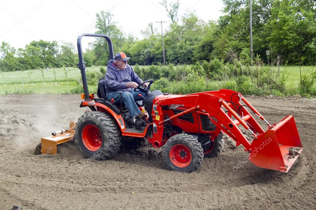 Older Farmer Tilling His Garden With A Small Tractor Stock Photo