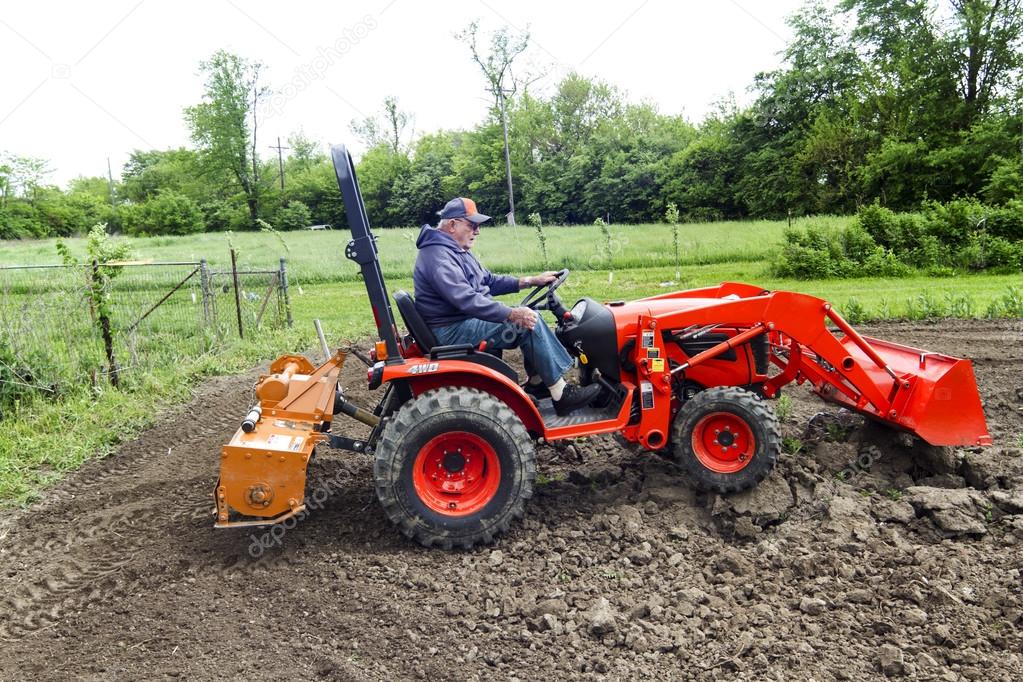 Older Farmer Tilling His Garden With A Small Tractor Stock Photo