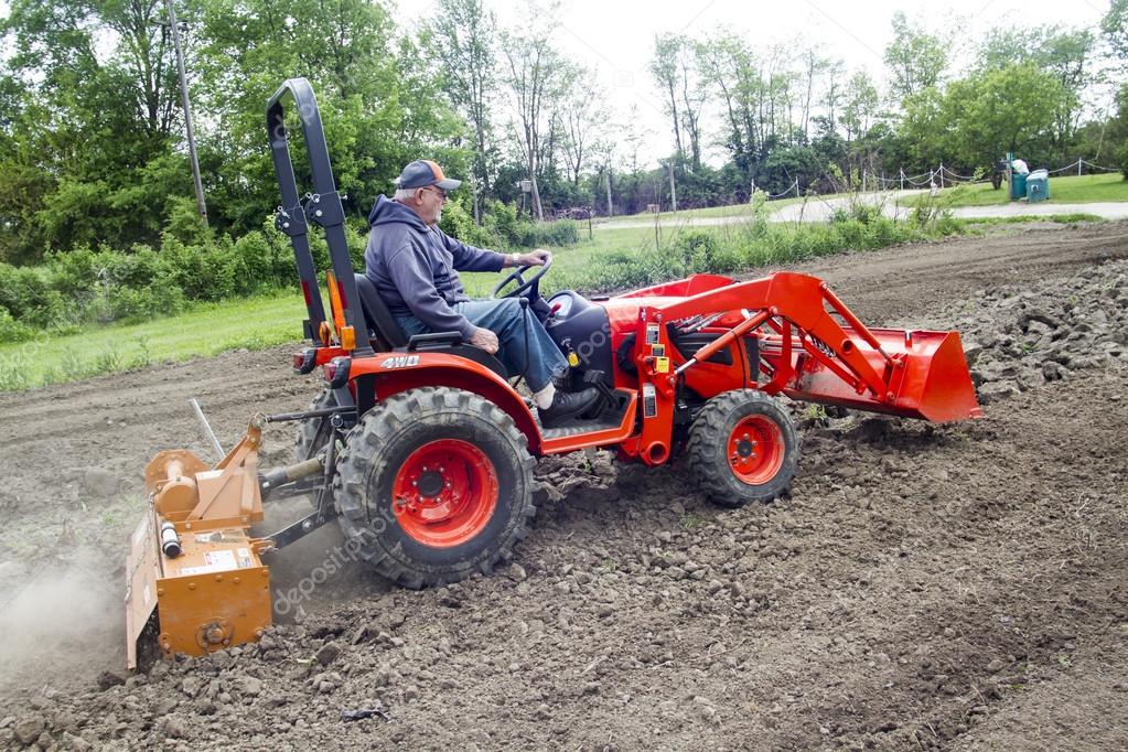 Older Farmer Tilling His Garden With A Compact 4x4 Tractor Stock