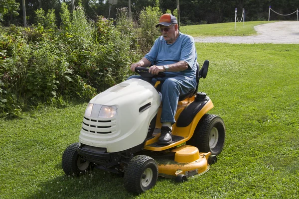 Maschio anziano falciatura erba con la sua falciatrice equitazione — Foto Stock