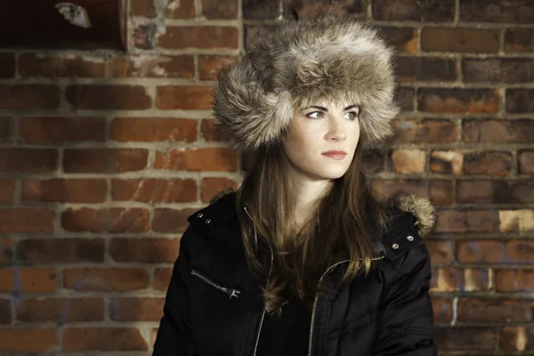 Ragazza che indossa peloso inverno cappello mattone muro sfondo — Foto Stock