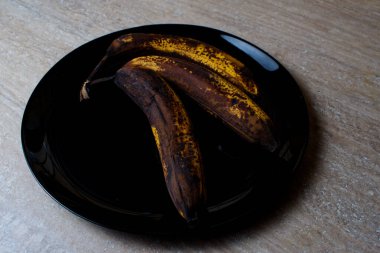 Siyah bir tabakta üç çürük muz. Çürümüş siyah muzlar.