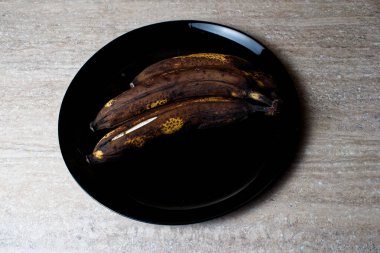 Siyah bir tabakta üç çürük muz. Çürümüş siyah muzlar.