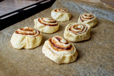 Çiğ tarçınlı çörekler. Pişirme kağıdında altı tane çözülmüş çörek. Pişirmeden önce hazırlama.