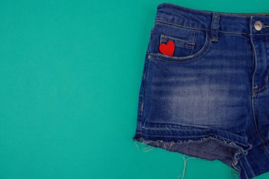 Mavi kot şortun yarısı mavi arkaplanda, cebinde boş alanın yanında kırmızı tahta bir kalp var.