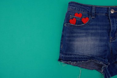 Mavi kot şortun yarısı mavi arkaplanda, cebinde üç tane tahta kalp var, boş alanın yanında.