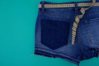 Mavi kot şortun yarısını mavi arka planda, boş bir alanın yanında kemer yerine bir santimetre ile kapat. Vücut ölçüm konsepti. Kıyafetler için ölçüler.