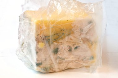 Spoiled cheese in a bag on a white plate. Decayed Cheese.