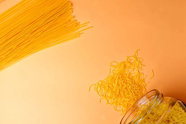 Scattered vermicelli on a peach background and spaghetti.